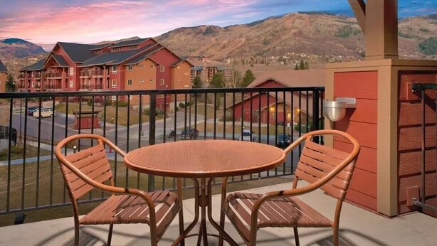 A balcony with a round table and two chairs, overlooking a residential area with red buildings and a mountainous backdrop. - 3BR, sleep 8, Club Wyndham, ski shuttle, pool, spa in Steamboat Springs (Steamboat Springs)