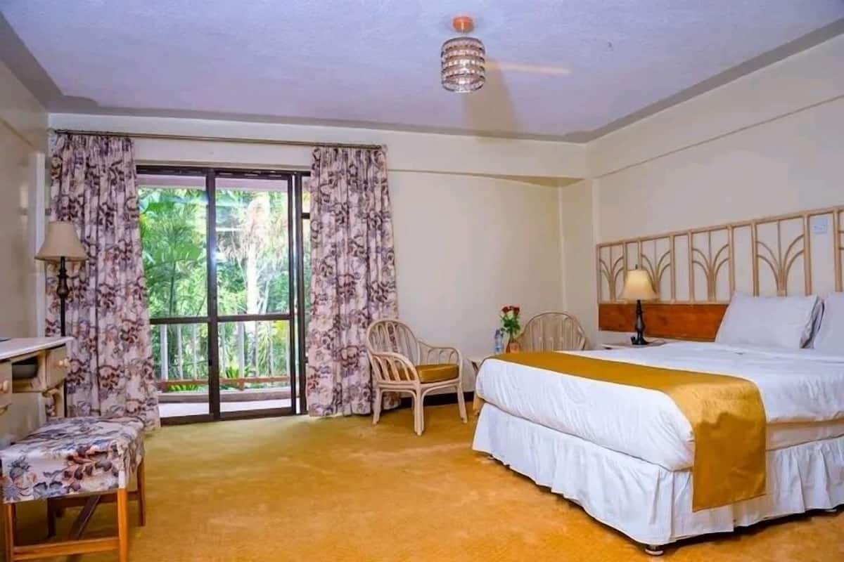 Ein Hotelzimmer mit Bett, Schreibtisch, Stuhl und einem großen Fenster mit Vorhängen.