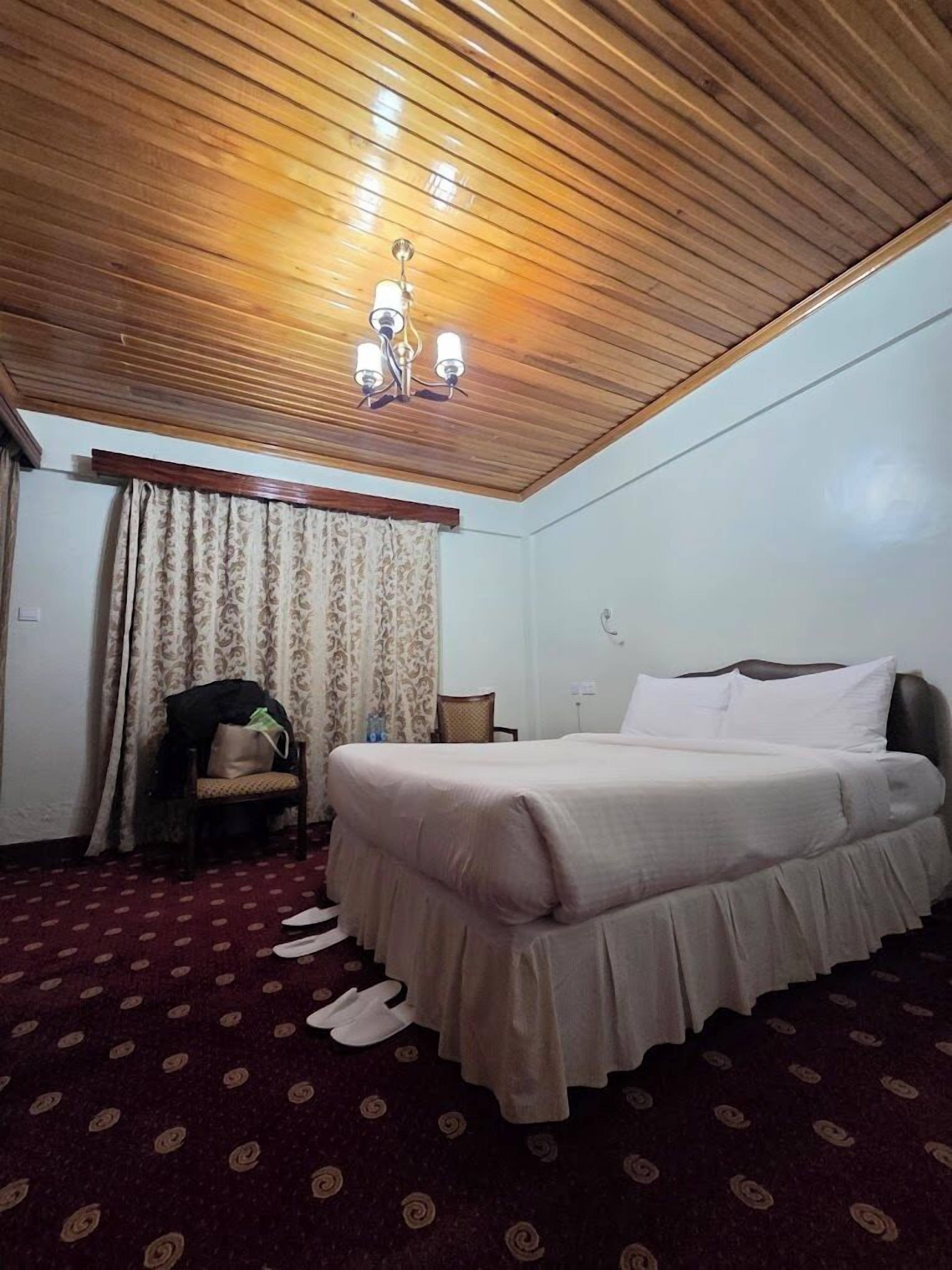 Une chambre d’hôtel avec un plafond en bois, un lit avec une literie blanche, une chaise et un tapis à motifs.
