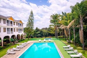 Un espace piscine avec des chaises longues, un bâtiment doté de balcons et une végétation tropicale.