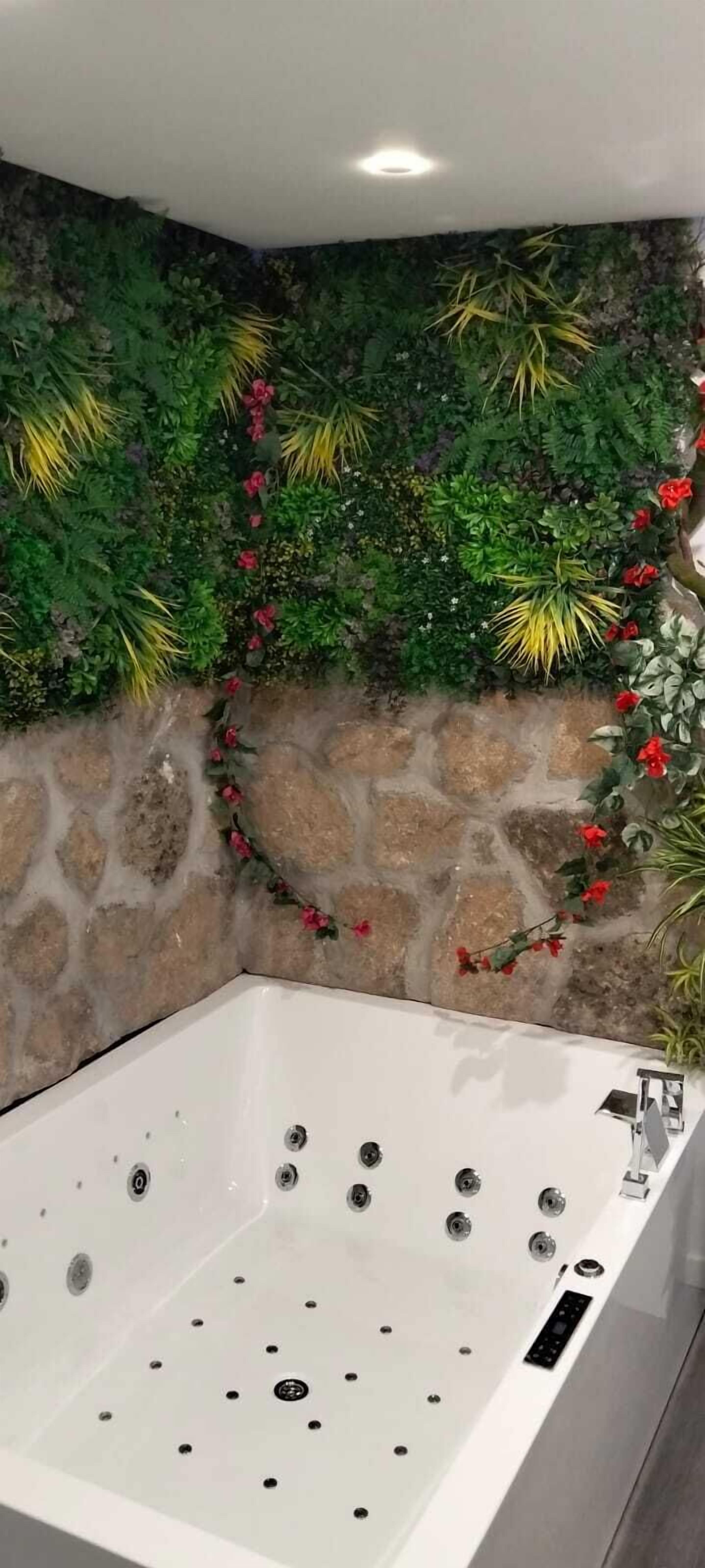 Une salle de bain avec un mur en pierre, une baignoire blanche et des éléments de décoration à base de feuillage vert.