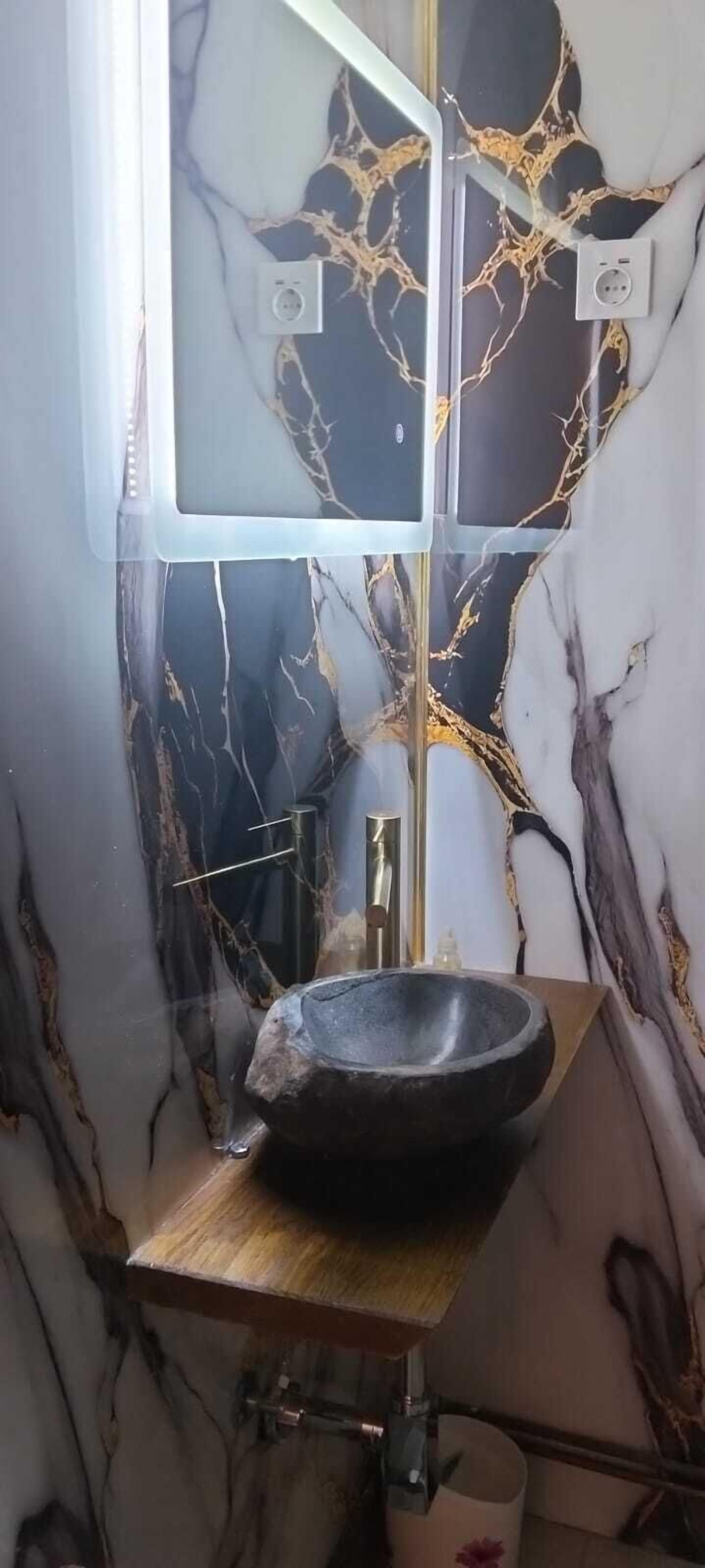 Un baño con pared de mármol, lavamanos negro y espejo.