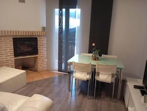 A living room with a fireplace, a dining table with chairs, a television, and a sliding glass door leading to a balcony.