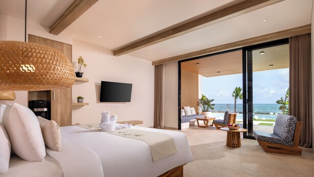 Habitación de hotel moderna con una cama grande, un televisor de pantalla plana, un balcón con asientos y vista al océano.
