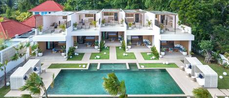 A modern multi-story building with a central swimming pool, surrounded by well-maintained lawns and potted plants.