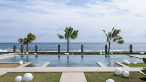 Zona de piscina con palmeras y vista al océano.