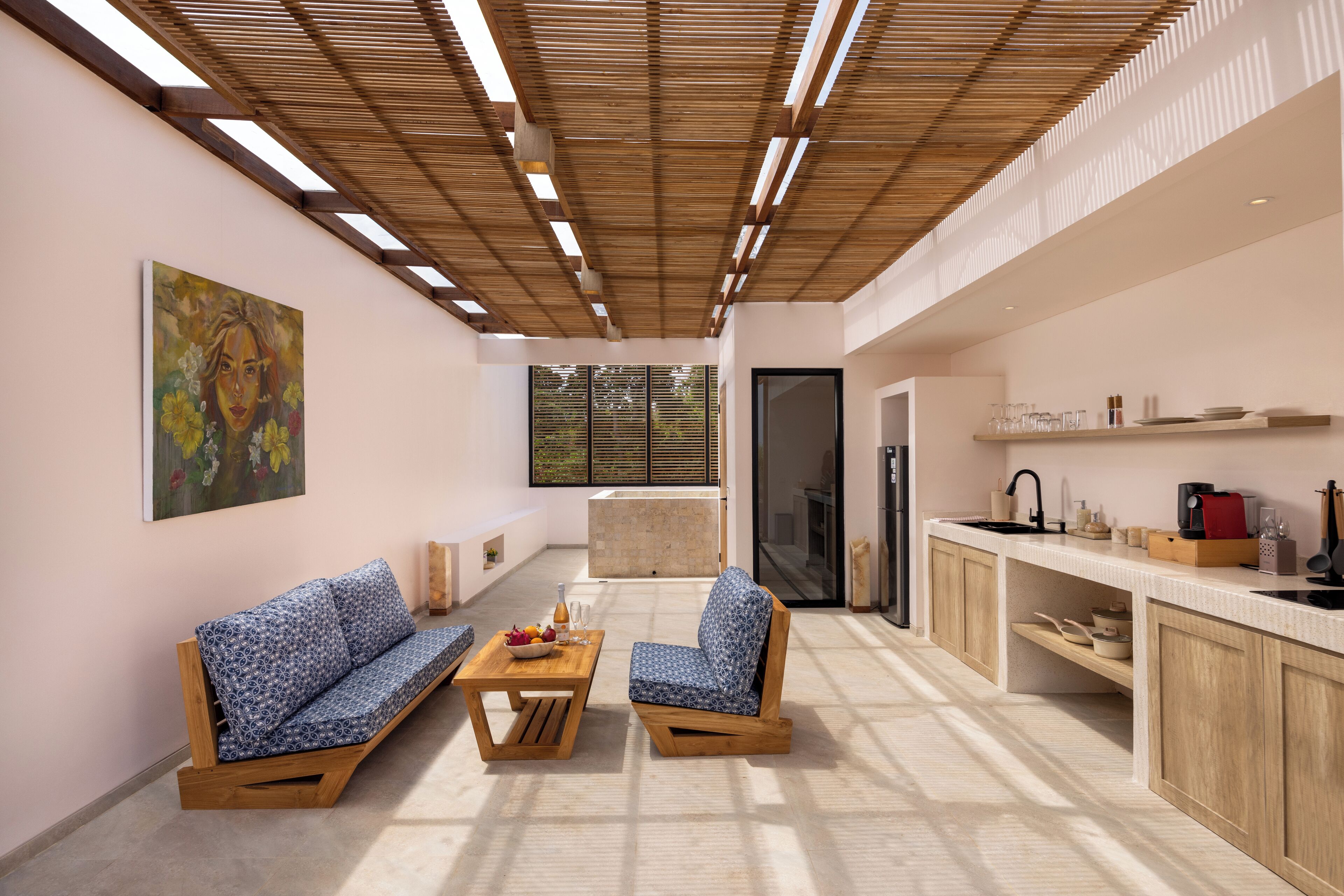A modern kitchen with wooden cabinets, a built-in oven, and a sink. There is a dining area with a sofa and a coffee table.