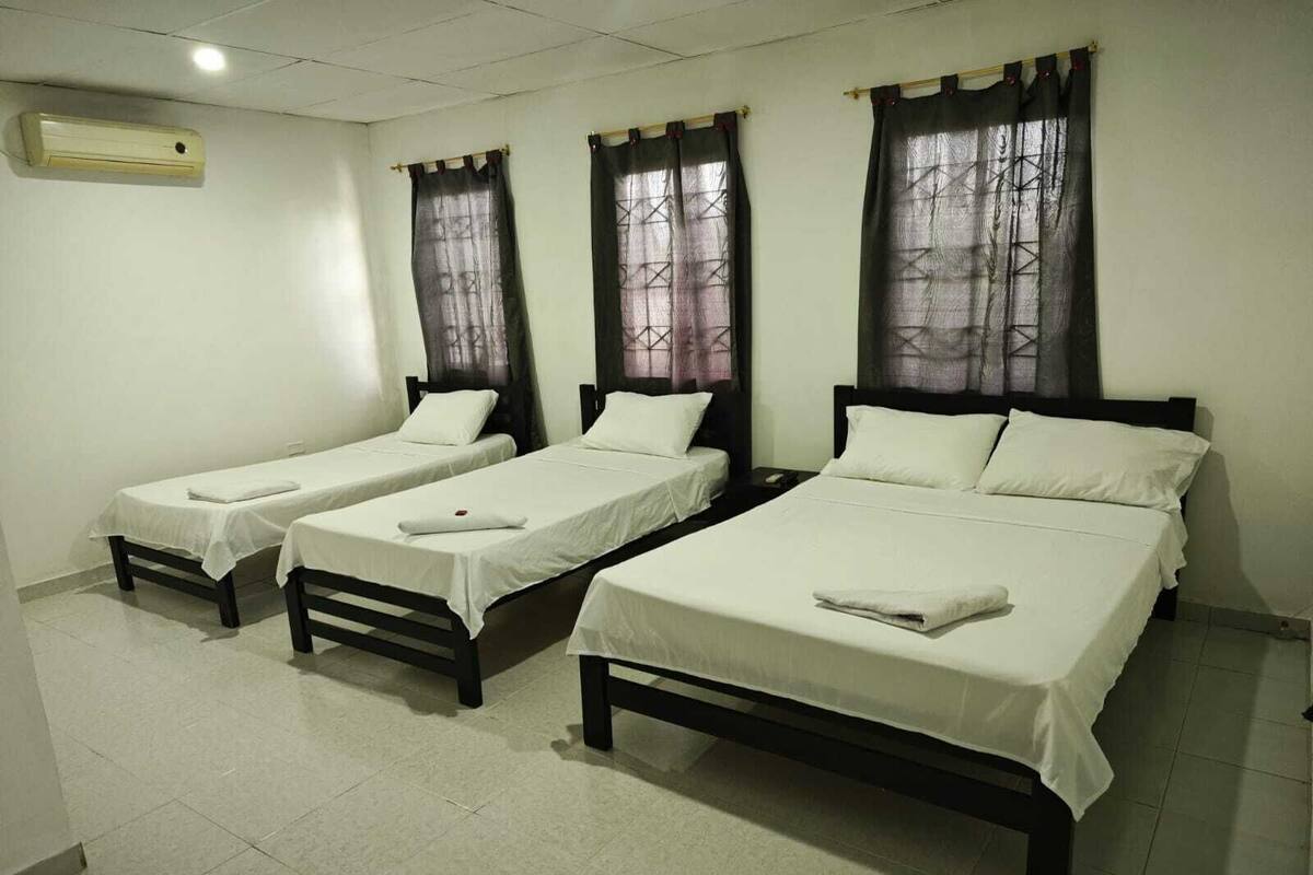 A hotel room with three single beds and one double bed, all with white linens.