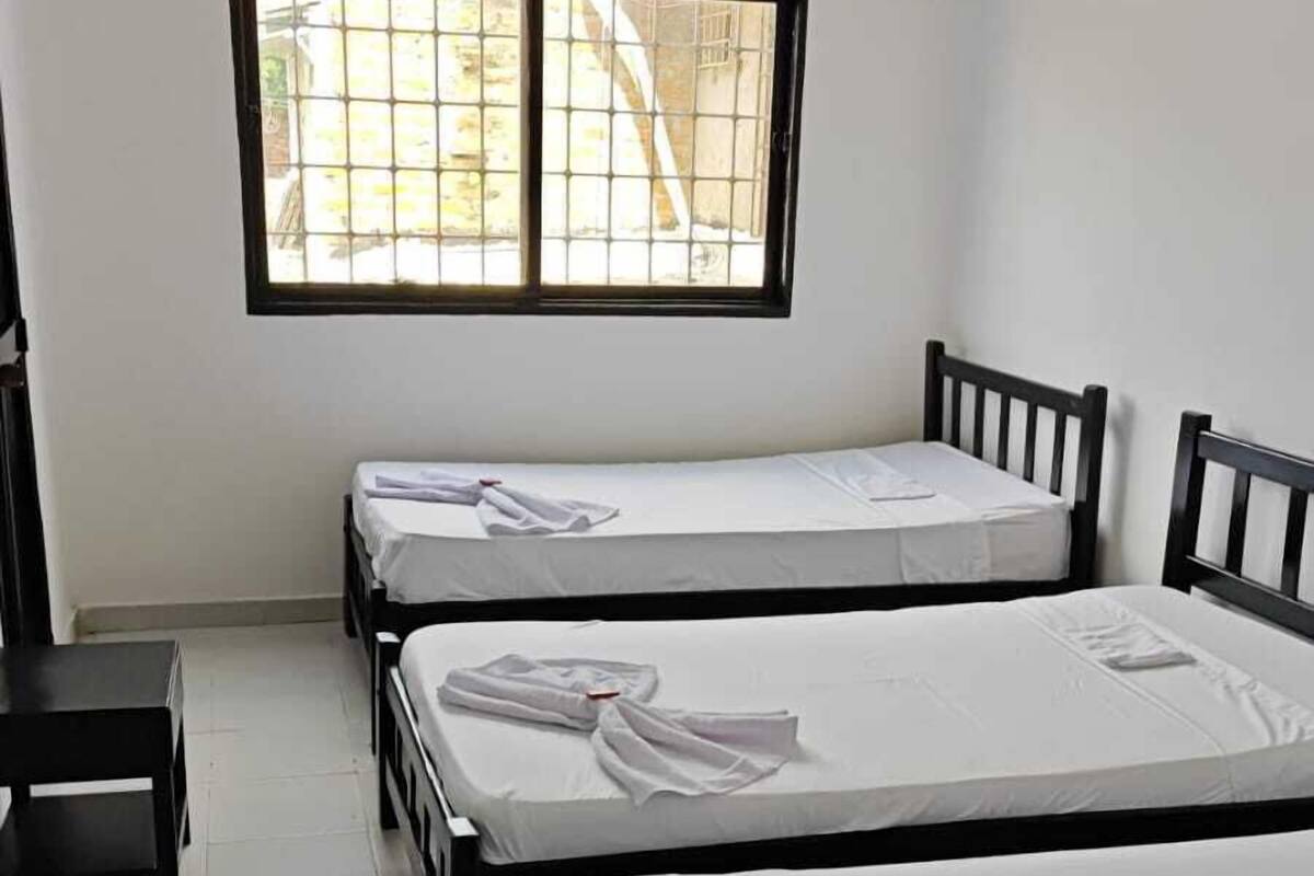 A hotel room with three single beds, a small table, and a window with a view of the outside.
