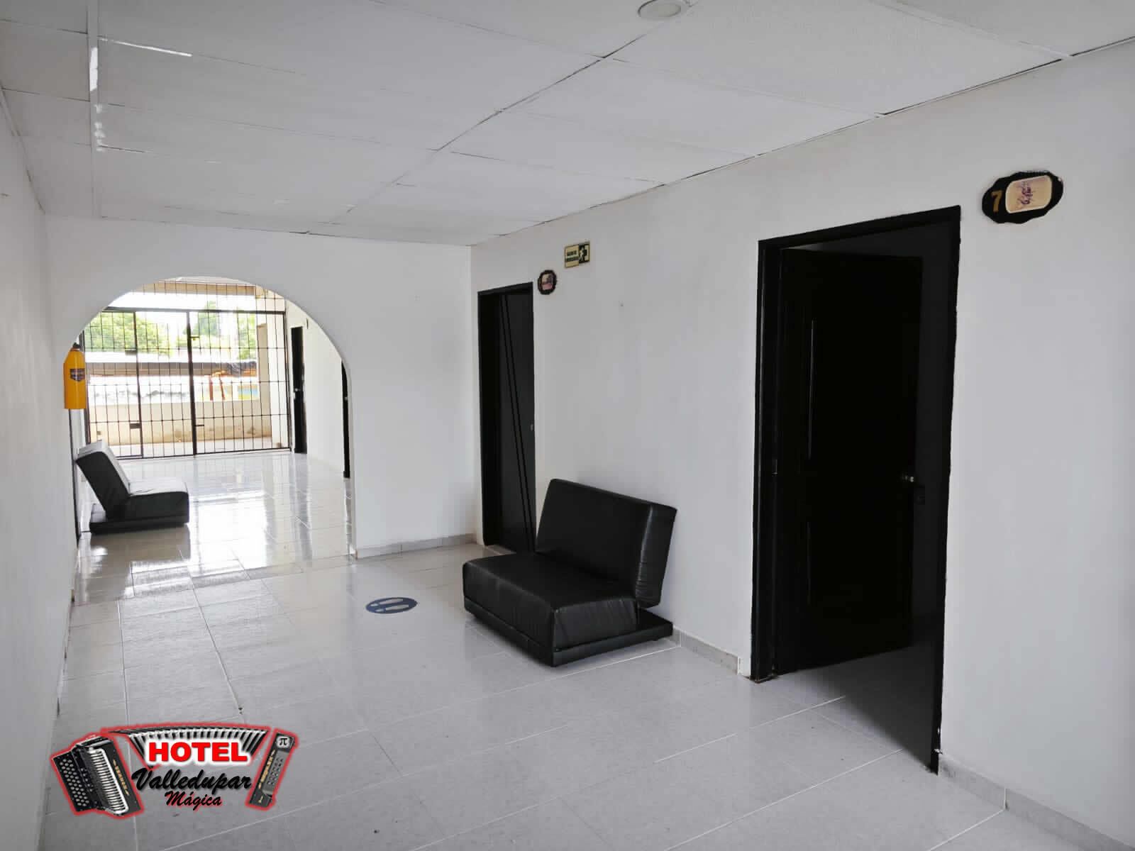 Un vestíbulo de hotel con piso de baldosas, una silla negra y una puerta negra.