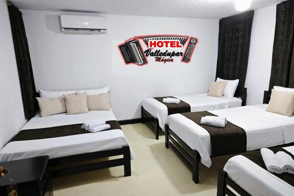 A hotel room with three beds, a small table, and an air conditioning unit on the wall.