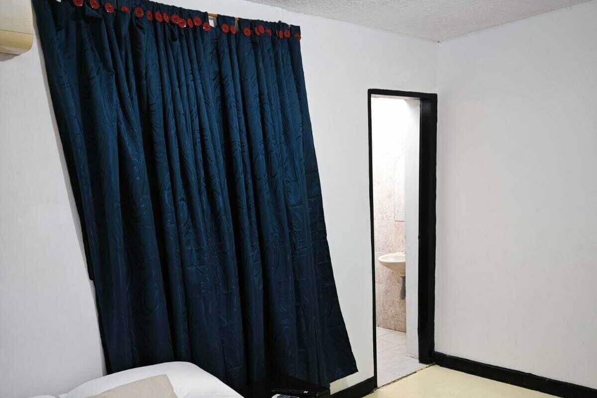 A hotel room with a bed, a nightstand, a remote control, and a bathroom visible through a door.