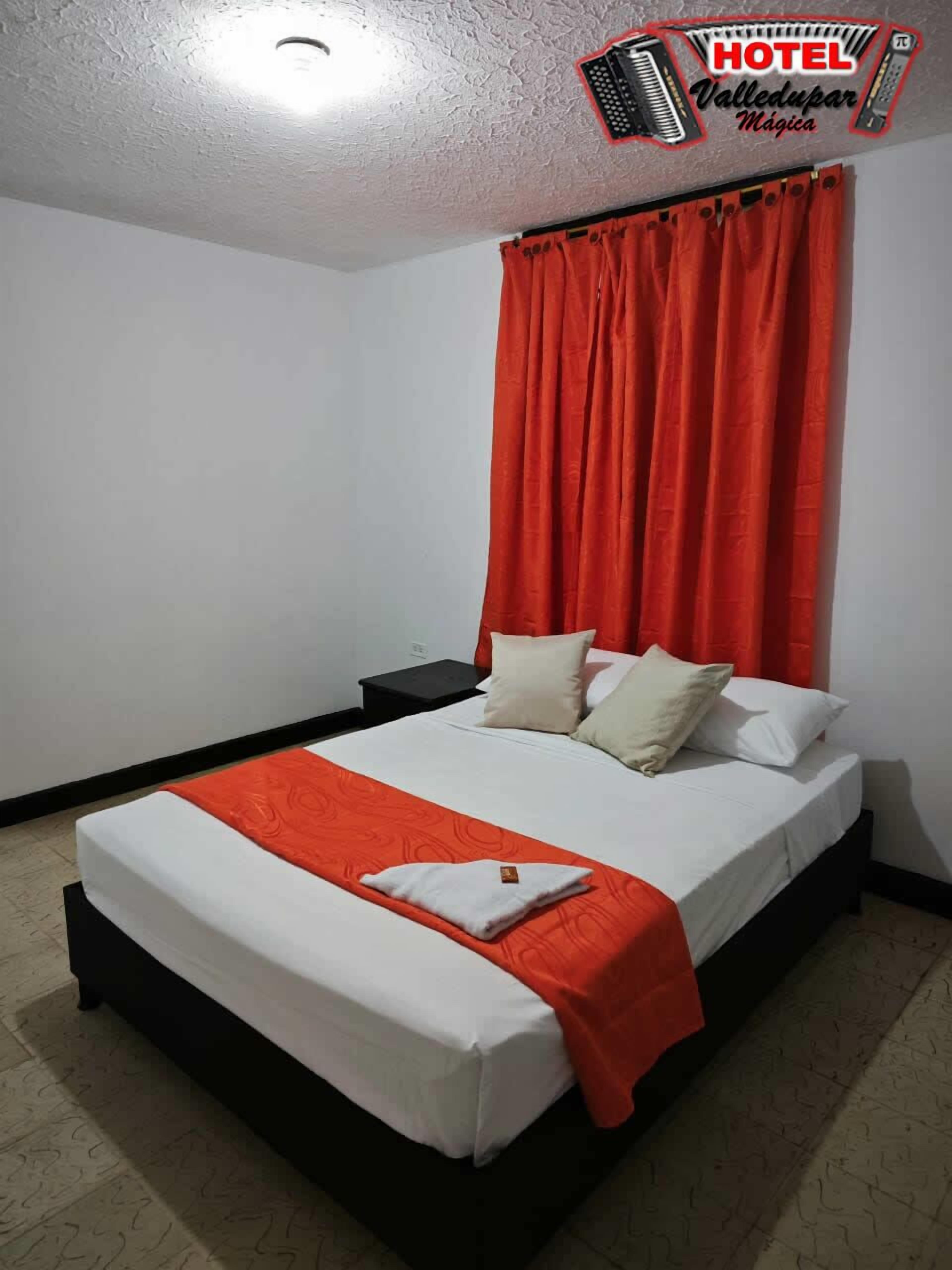 Una habitación de hotel con una cama individual, ropa de cama blanca, una cortina roja y una mesita de noche pequeña.