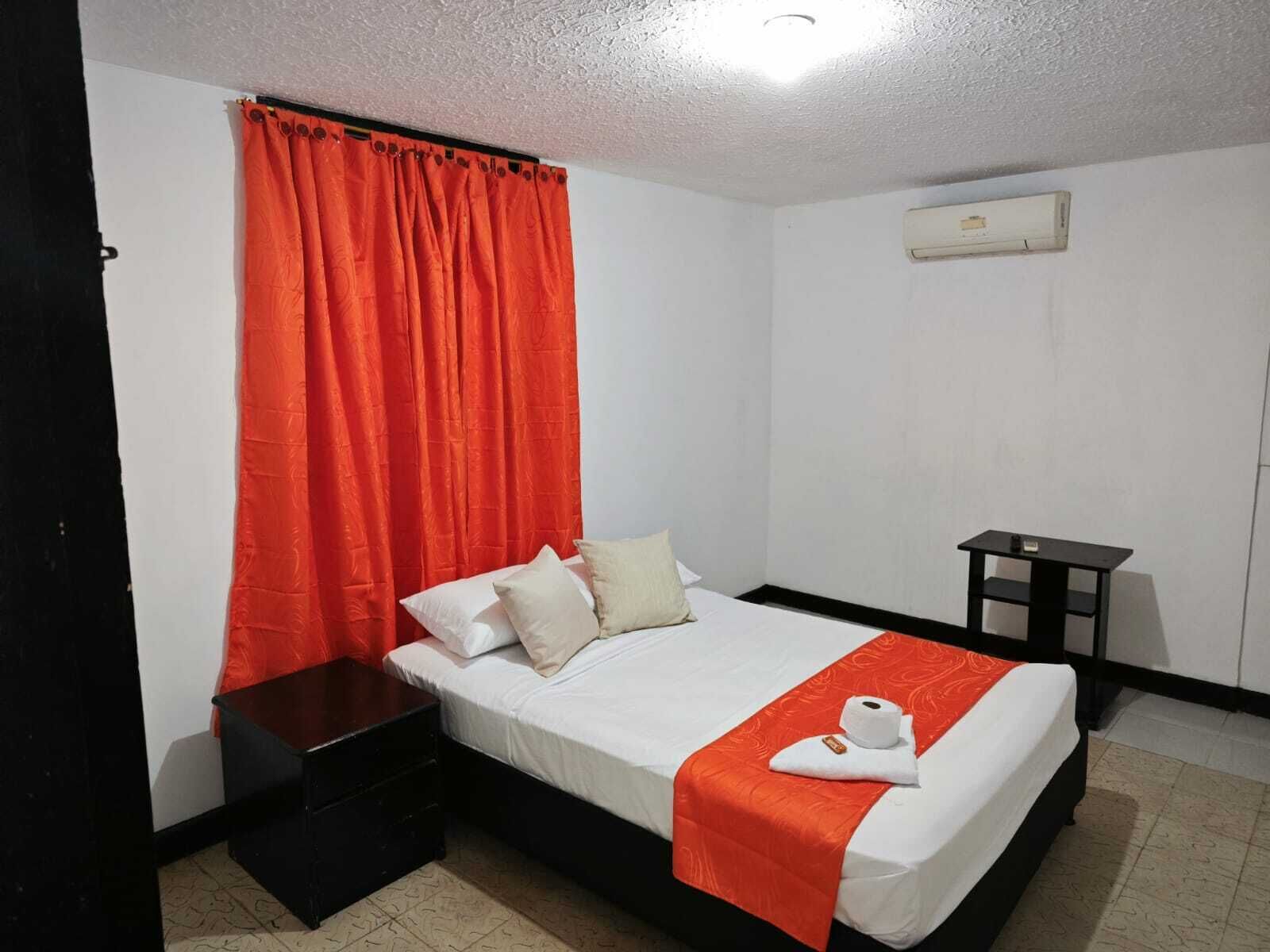 Habitación de hotel con cama, mesita de noche, una pequeña mesa y aire acondicionado de pared.