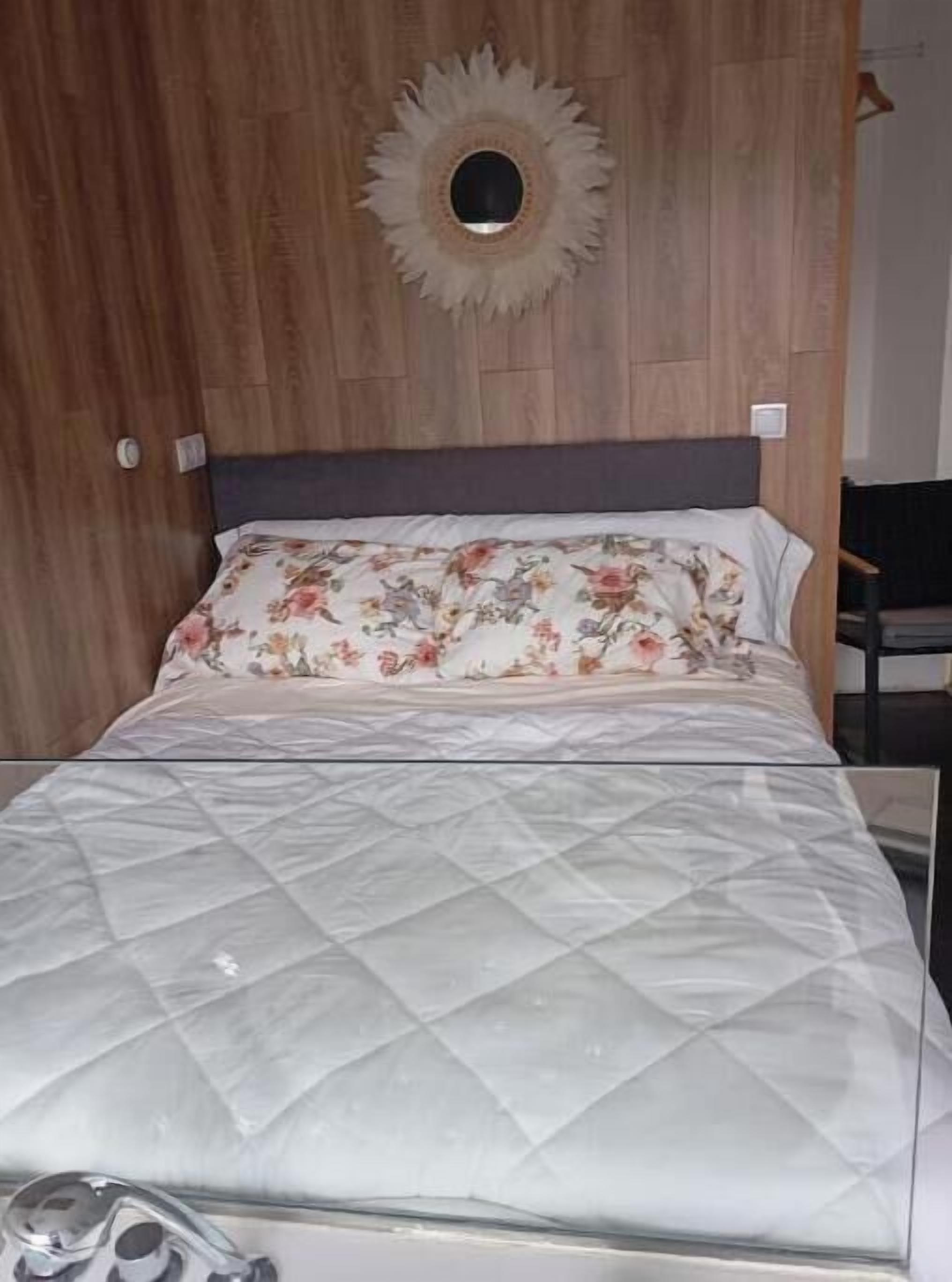 Una cama con colchón acolchado, almohada estampada y un espejo circular fijado a la pared.