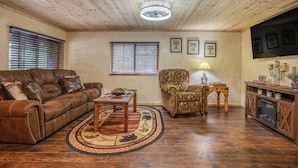 A living room with a leather sofa, patterned armchair, wooden coffee table, and a rug. - Outlaw Cabin - Newly Renovated, Covered Deck, Tons of Wildlife (Ruidoso)