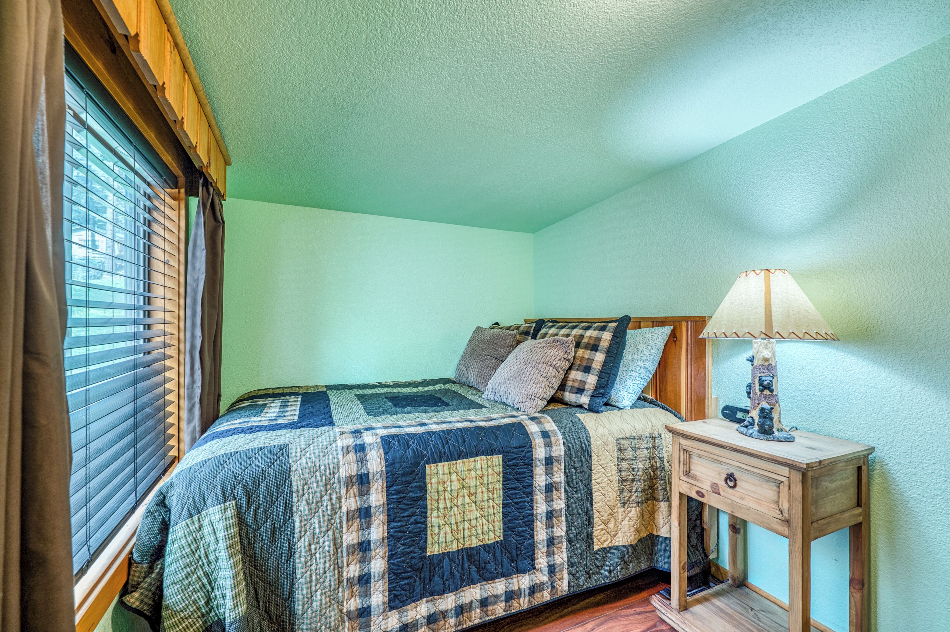 A bedroom with a bed, a nightstand, a lamp, and a window with blinds.