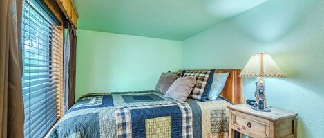 A bedroom with a bed, a nightstand, a lamp, and a window with blinds.