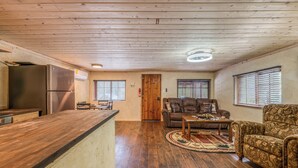 A spacious living area with a wooden ceiling, a kitchen with a stainless steel refrigerator, and a cozy seating area with a patterned sofa and a coffee table. - Outlaw Cabin - Newly Renovated, Covered Deck, Tons of Wildlife (Ruidoso)