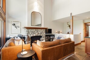 Un salon moderne avec une cheminée en pierre, des canapés en cuir, une table basse ronde et un téléviseur à écran plat.
