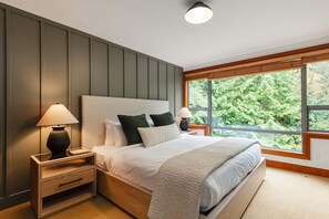 Une chambre à coucher avec un grand lit, deux tables de chevet, une commode et une fenêtre donnant sur des arbres.