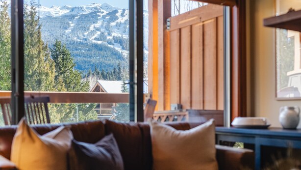 Ein gemütliches Wohnzimmer mit einer Ledersofa und Blick auf schneebedeckte Berge durch große Fenster.