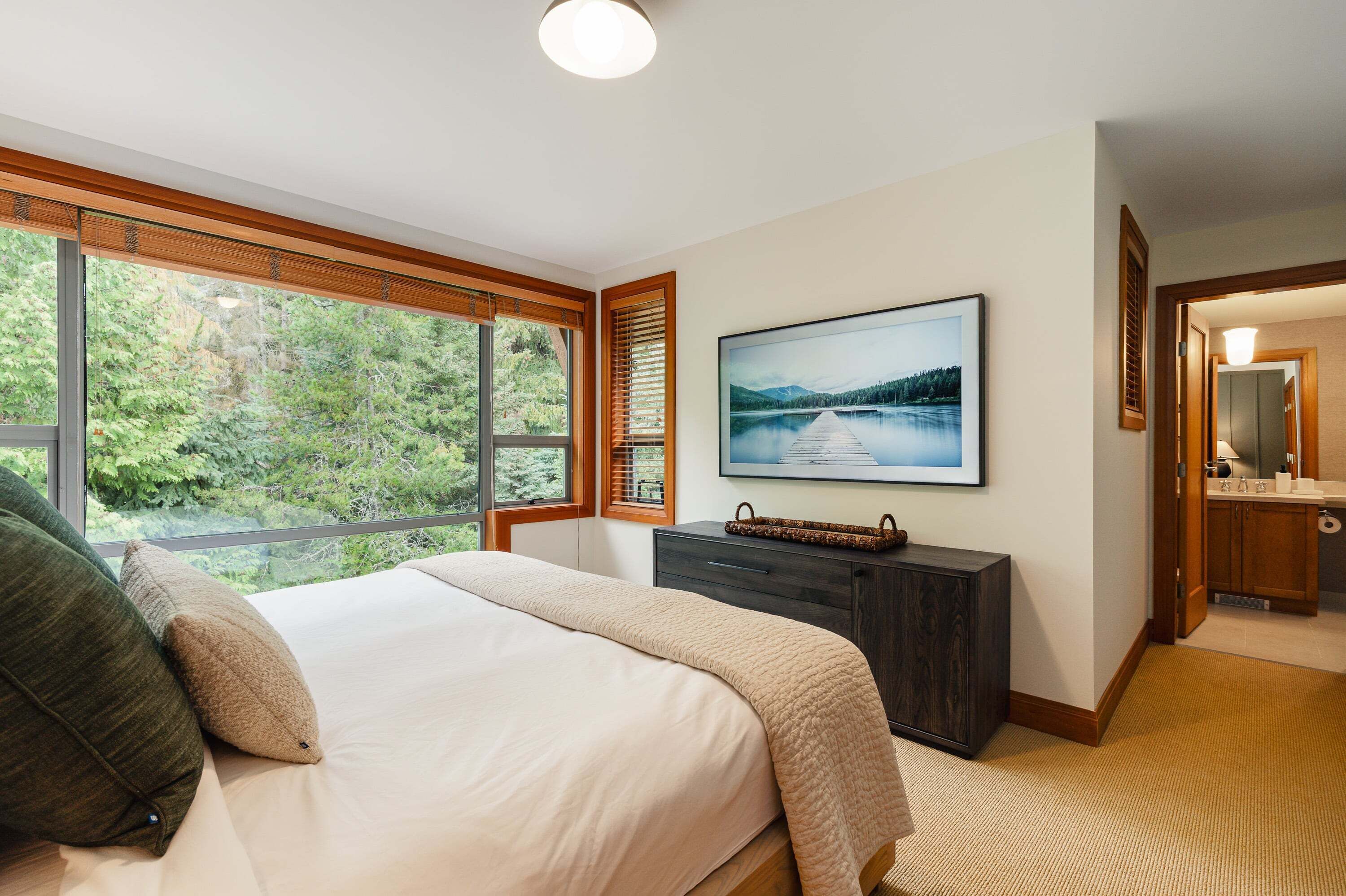 Una camera da letto con un letto grande, una cassettiera, un quadro incorniciato e vista sugli alberi dalla finestra.