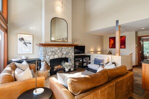 Un vaste salon doté d’une cheminée en pierre, de canapés en cuir, d’un téléviseur à écran plat et d’un mur d’accent en pierre.