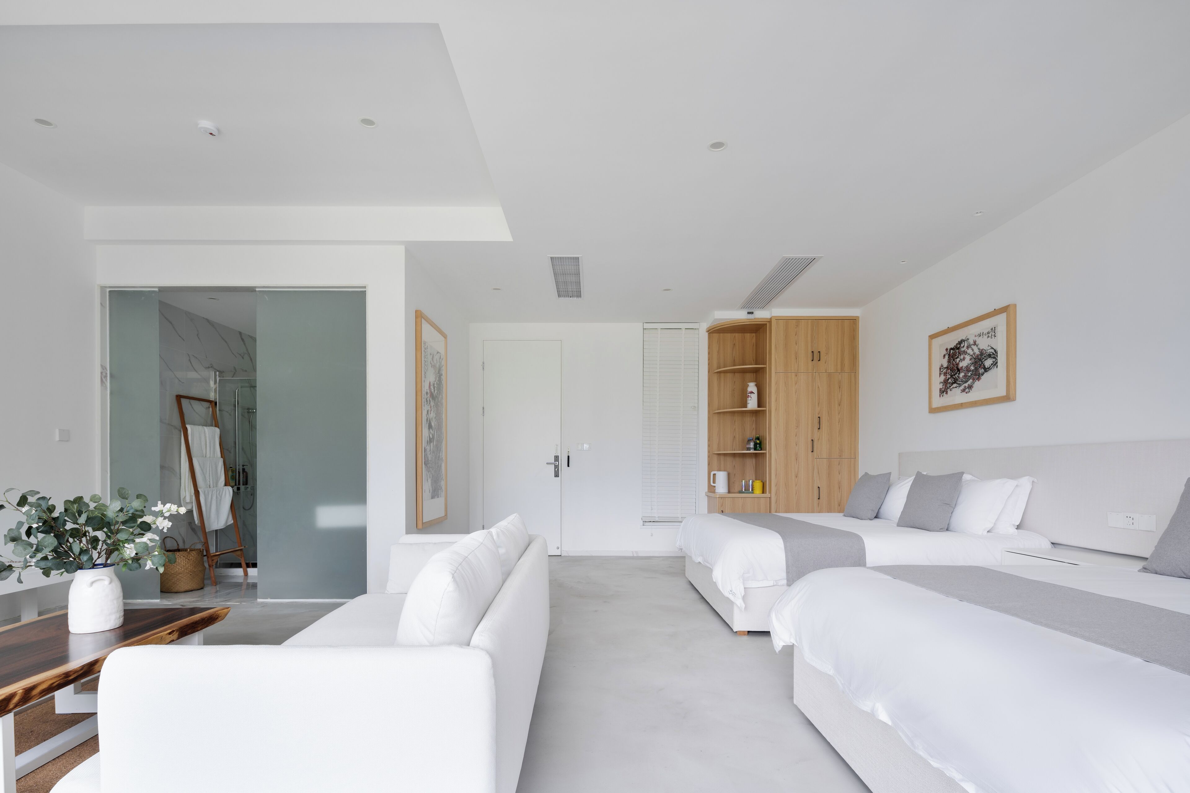 Una habitación de hotel moderna con una cama grande, una cama más pequeña, un sofá y un armario de madera.