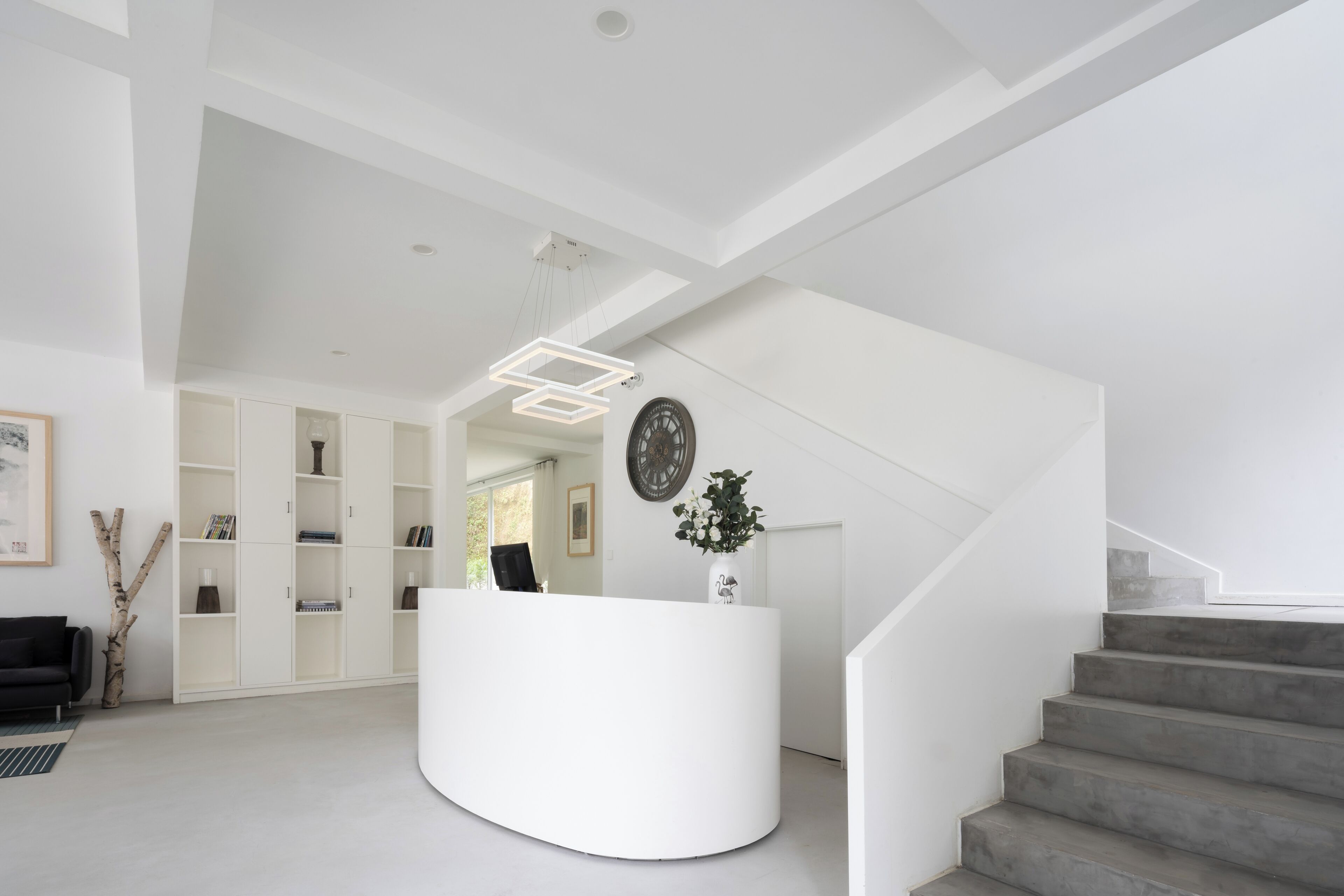 Un área de recepción moderna con un mostrador blanco, una escalera y una estantería.