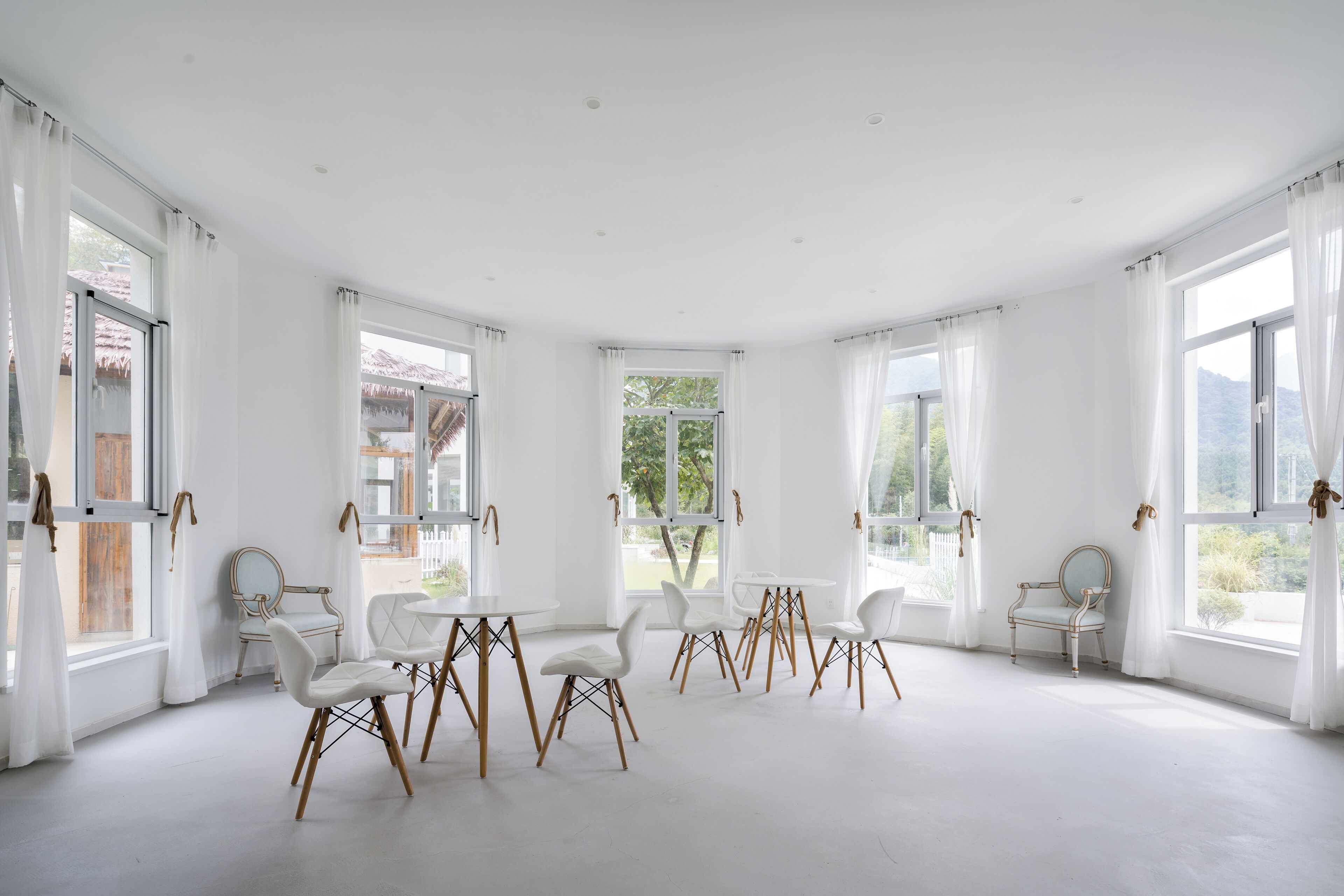 A spacious room with large windows, white walls, and a round table with chairs.