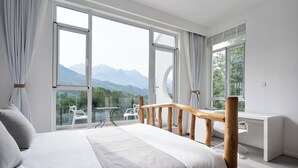 A bedroom with a large bed, a desk, and a view of mountains through large windows. - daiyungui (Huangshan)