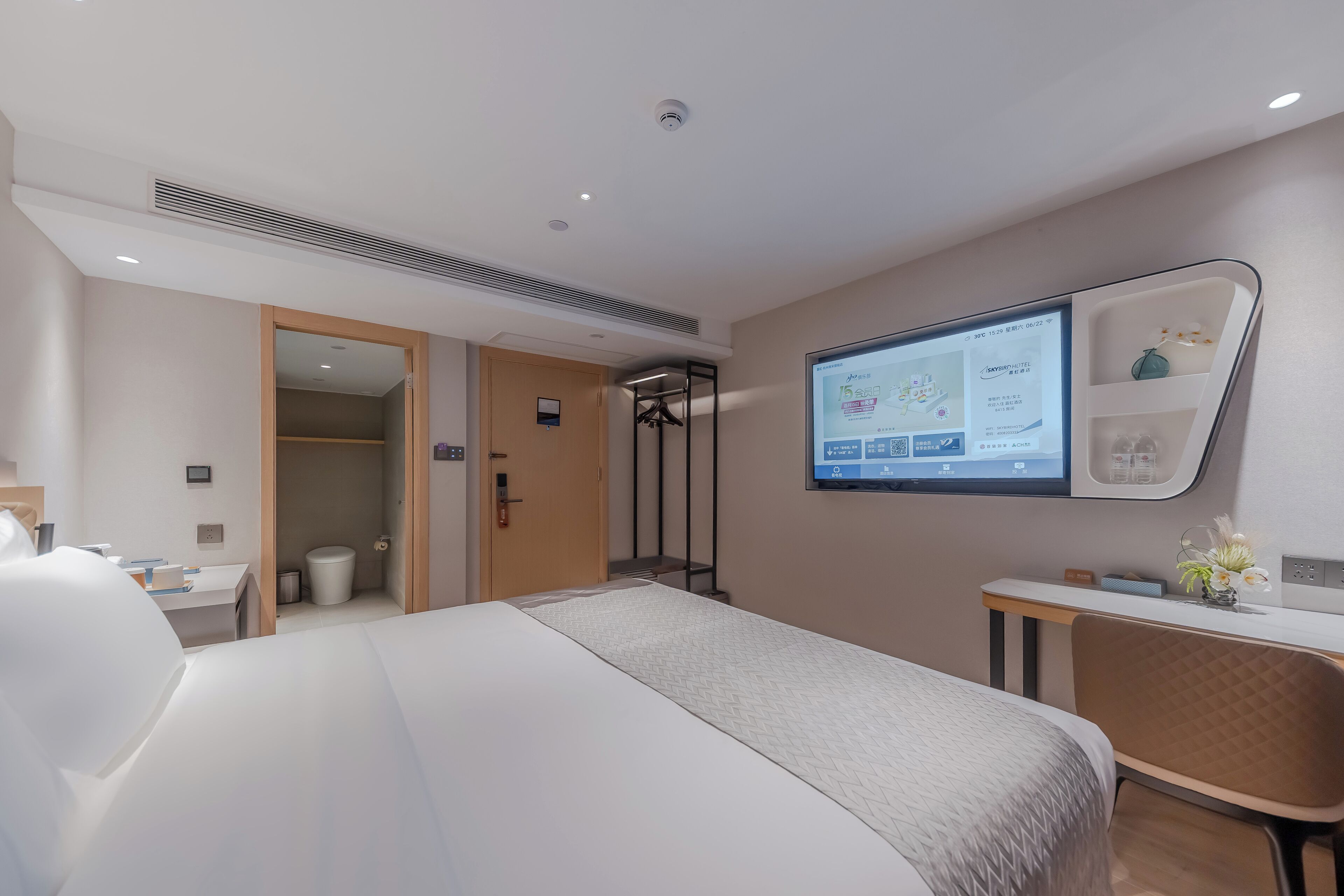 A modern hotel room with a large bed, a desk, a chair, and a wall-mounted TV displaying a map.