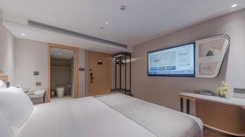 A modern hotel room with a large bed, a desk, a chair, and a wall-mounted TV displaying a map.