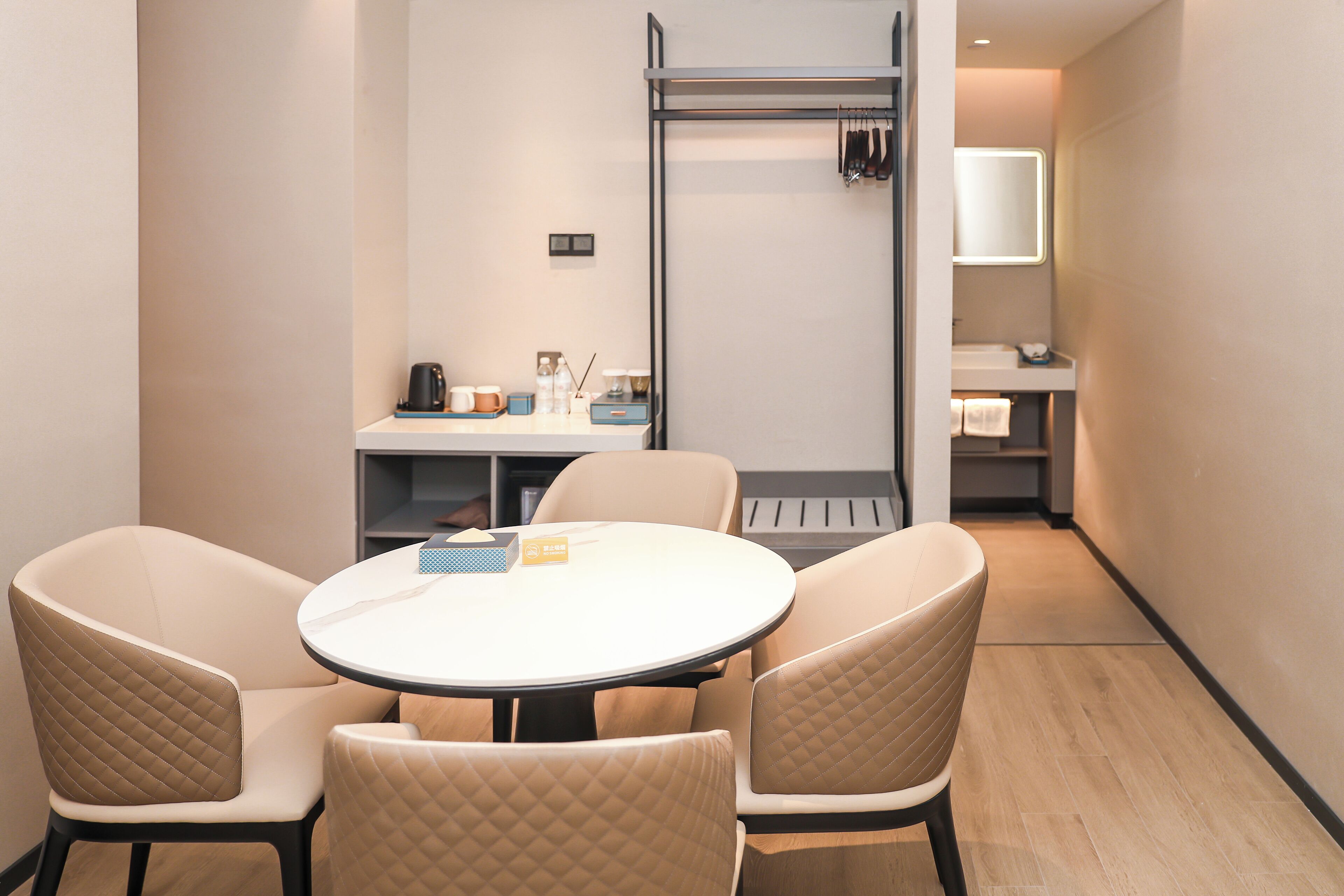 Hotelkamer met een ronde tafel en vier stoelen, een kitchenette, een spiegel en een kleine badkamer.