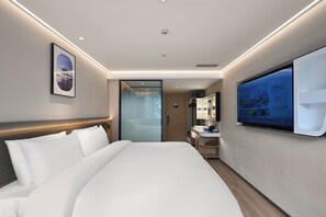 A modern hotel room with a large bed, a digital screen displaying information, a bathroom with a sink and mirror, and a door leading to a balcony. - SKYBIRD Hotel (Hangzhou)