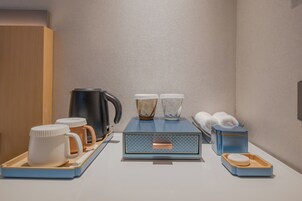 Habitación de hotel ordenada con una estación de café, un hervidor, dos tazas, una bandeja, una caja y un pequeño recipiente.