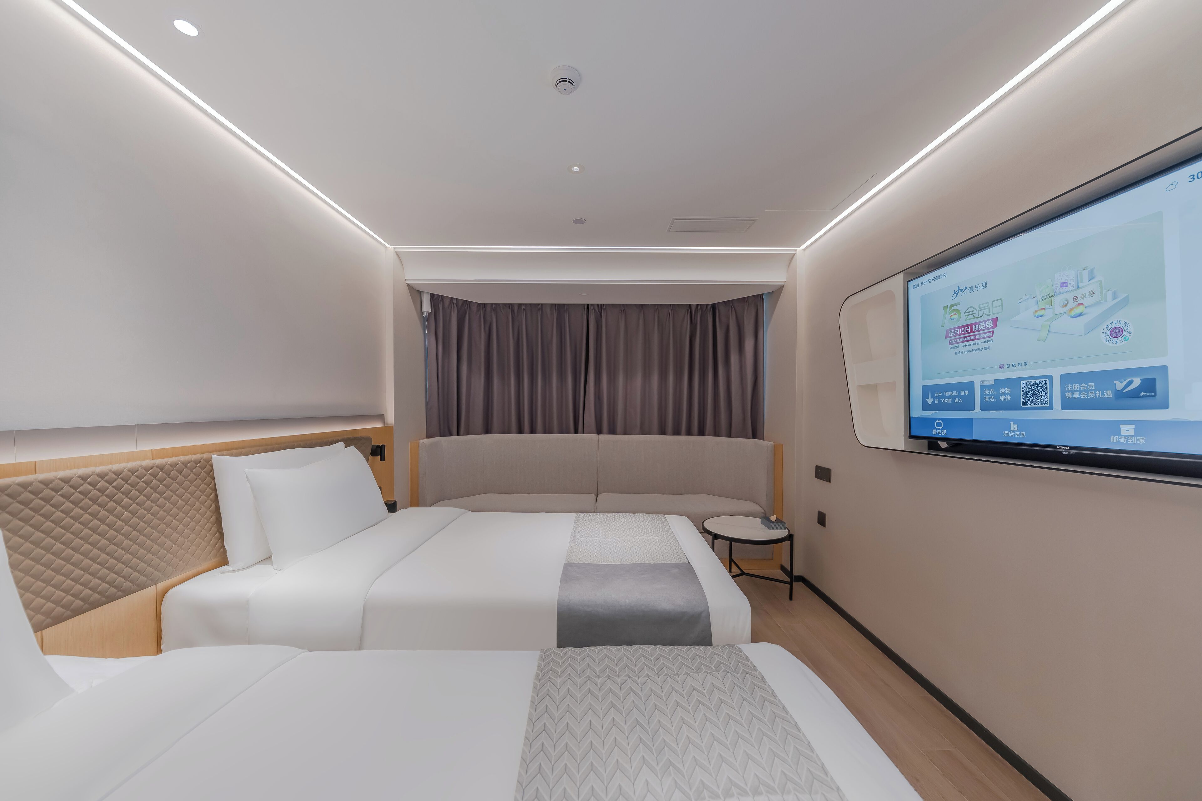 Ein modernes Hotelzimmer mit einem großen Bett, einem kleineren Bett, einem an der Wand montierten Fernseher und einem kleinen Tisch.