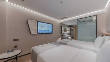 Una habitación de hotel moderna con dos camas, una mesita pequeña, un televisor montado en la pared y un separador de vidrio.