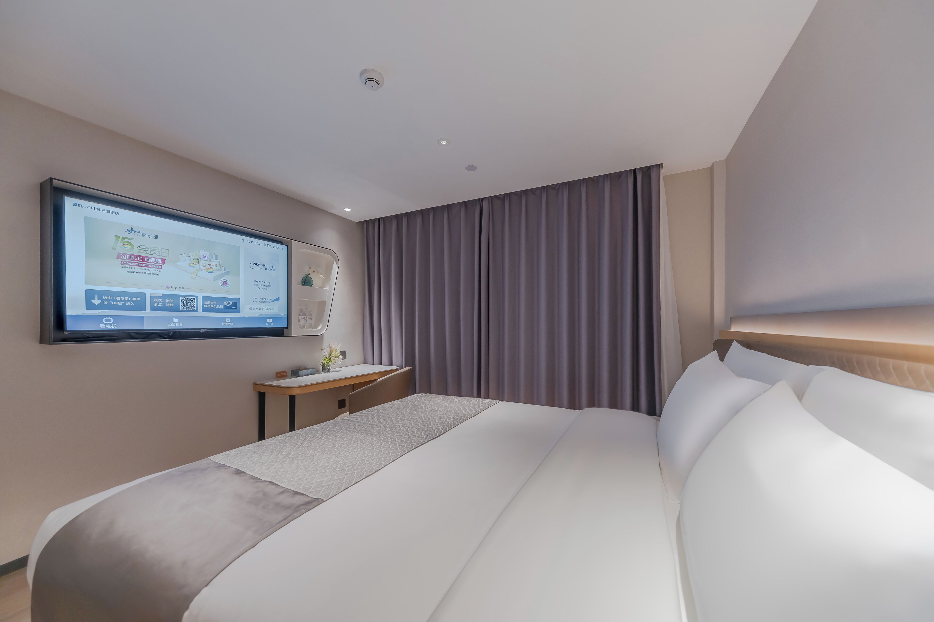 A hotel room with a large bed, a desk, a flat-screen TV mounted on the wall, and a window with curtains.