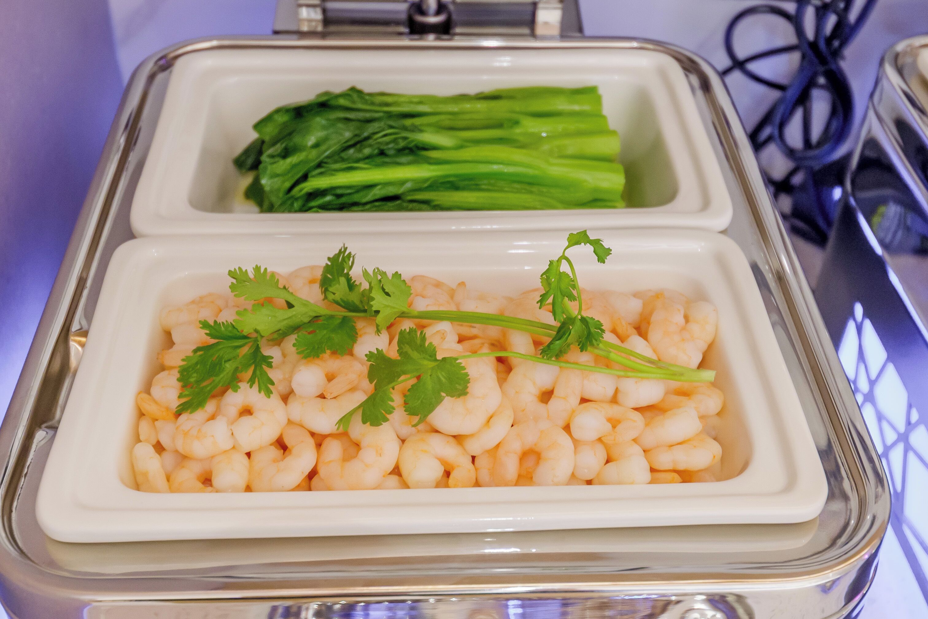 Un puesto de comida con dos compartimentos: uno con camarones y el otro con verduras verdes.