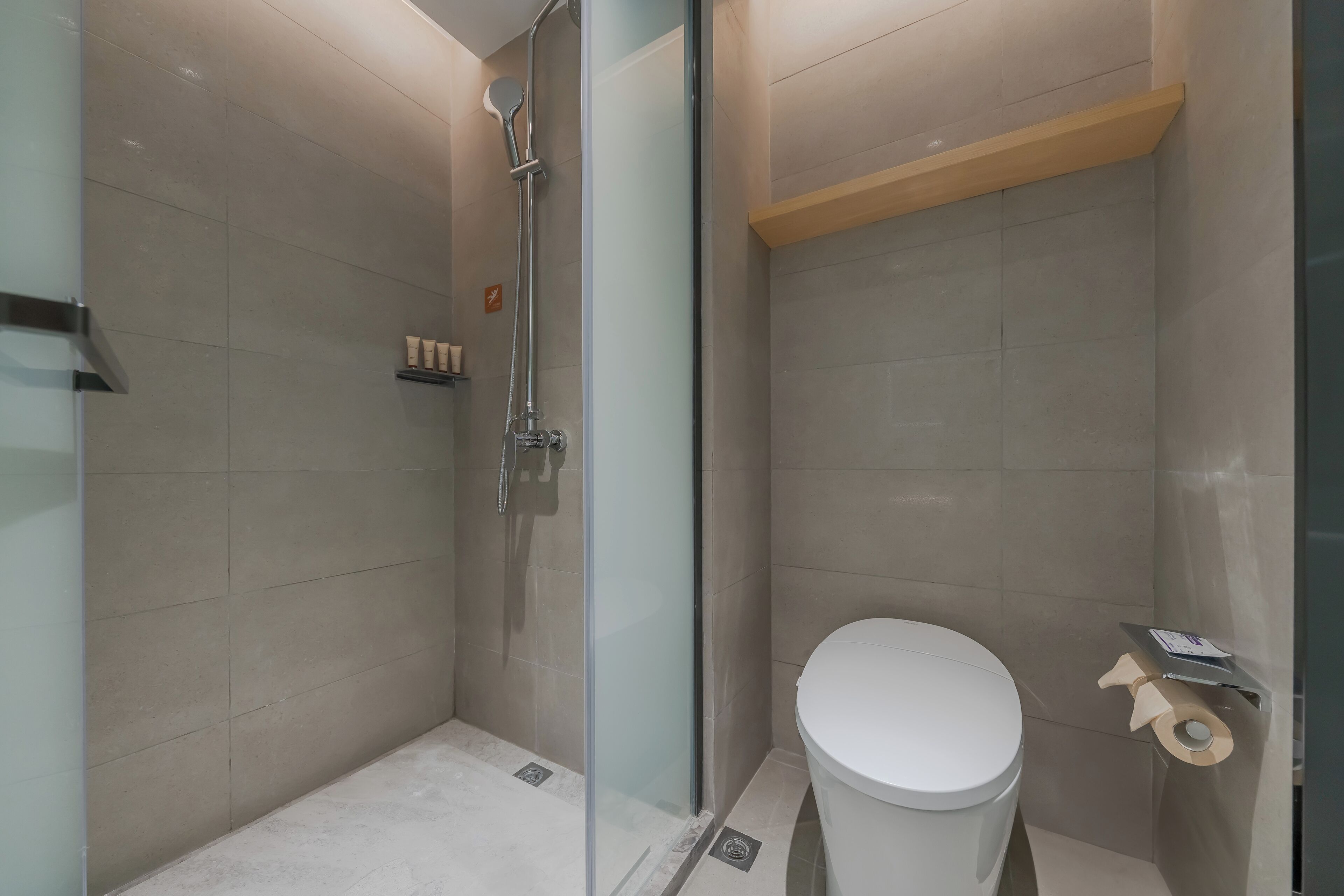 Un baño moderno con cabina de ducha de vidrio, inodoro blanco y estante de madera sobre el inodoro.