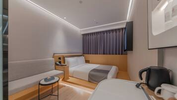 A modern hotel room with a bed, a sofa, a small table, a coffee maker, and a TV on the wall.