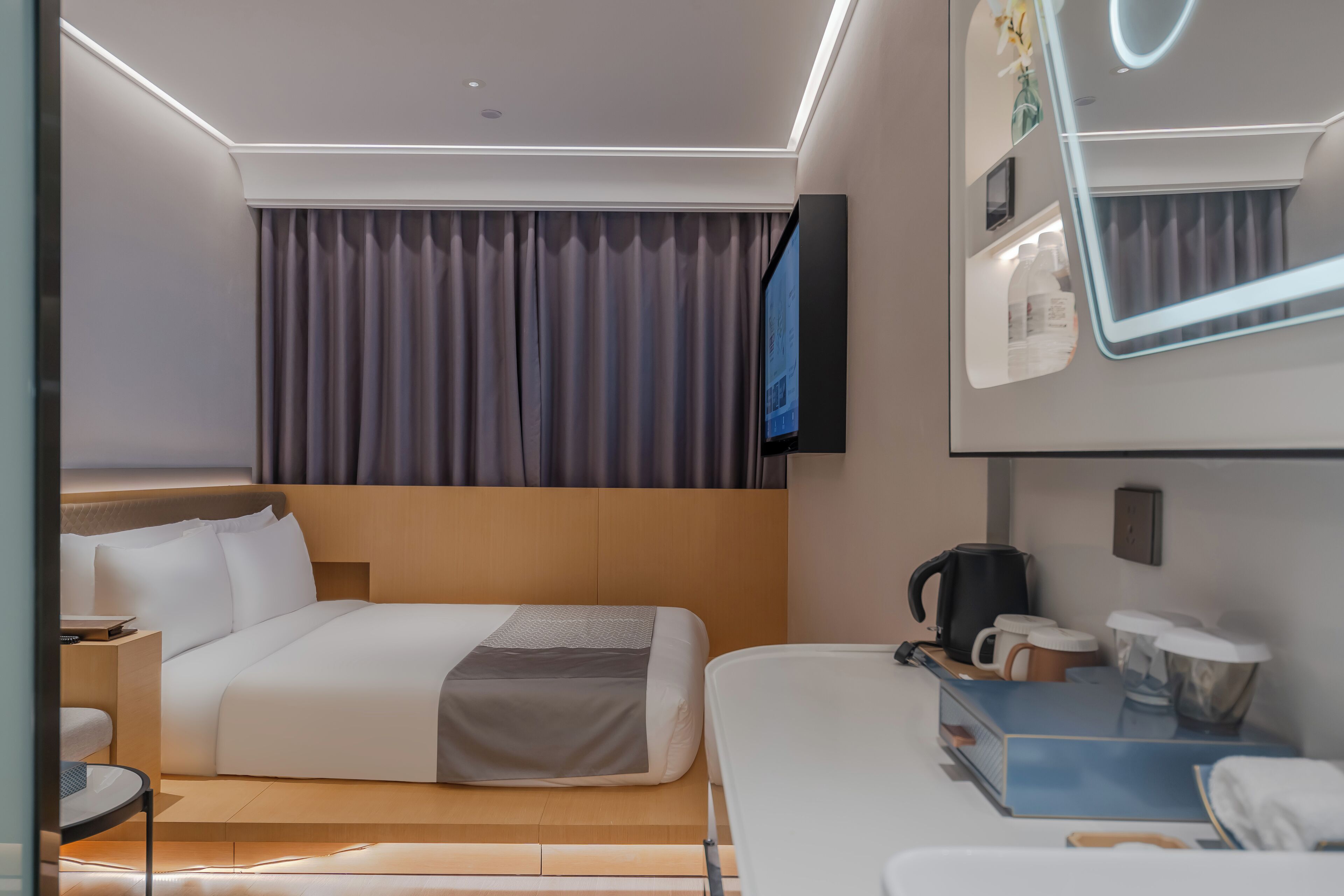 A modern hotel room with a large bed, a bedside table, a coffee maker, and a mirror.