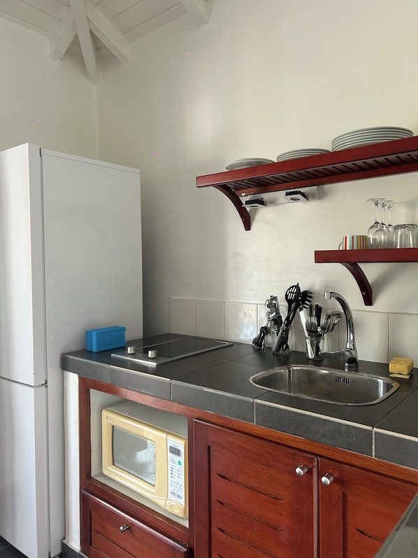A compact kitchen with a refrigerator, microwave, sink, and wooden cabinets.