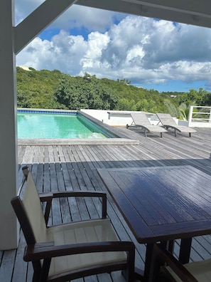 A wooden deck with a pool and lounge chairs overlooking a lush green landscape.