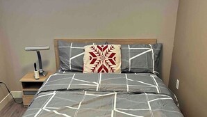 A modern bedroom with a bed, a nightstand, a lamp, and a window.
