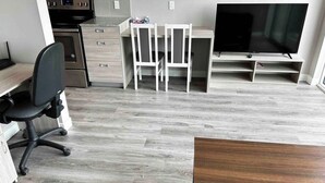 A compact kitchen with modern appliances, a dining area with a TV, and a workspace with a chair and desk.
