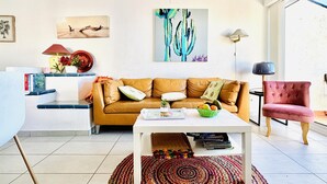 Ein Wohnzimmer mit einem braunen Ledersofa, einem weißen Couchtisch, einem farbenfrohen Teppich und einem rosafarbenen Sessel.