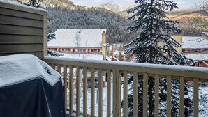 En balkon med udsigt over et sneklædt bjerglandskab, et overdækket udendørs opholdsområde og en bygning med rødt tag i baggrunden.
